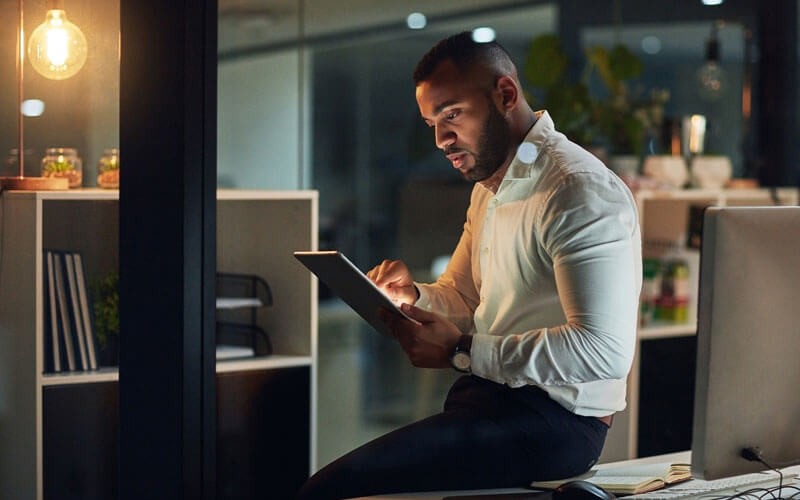 Business professional working remotely on tablet at night