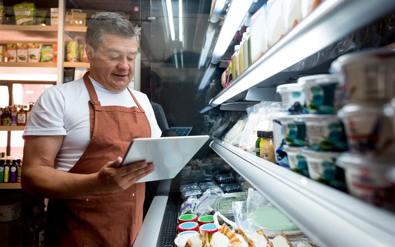 Grocer views information about food safety on tablet while in front of products