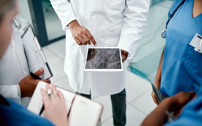 Doctors and nurses gathered around tablet displaying patient MRI results