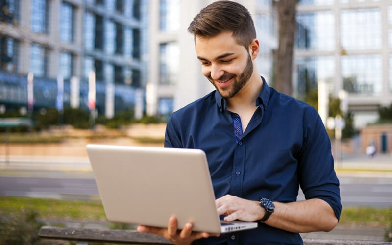 Smiling man on laptop computer sitting outside in city